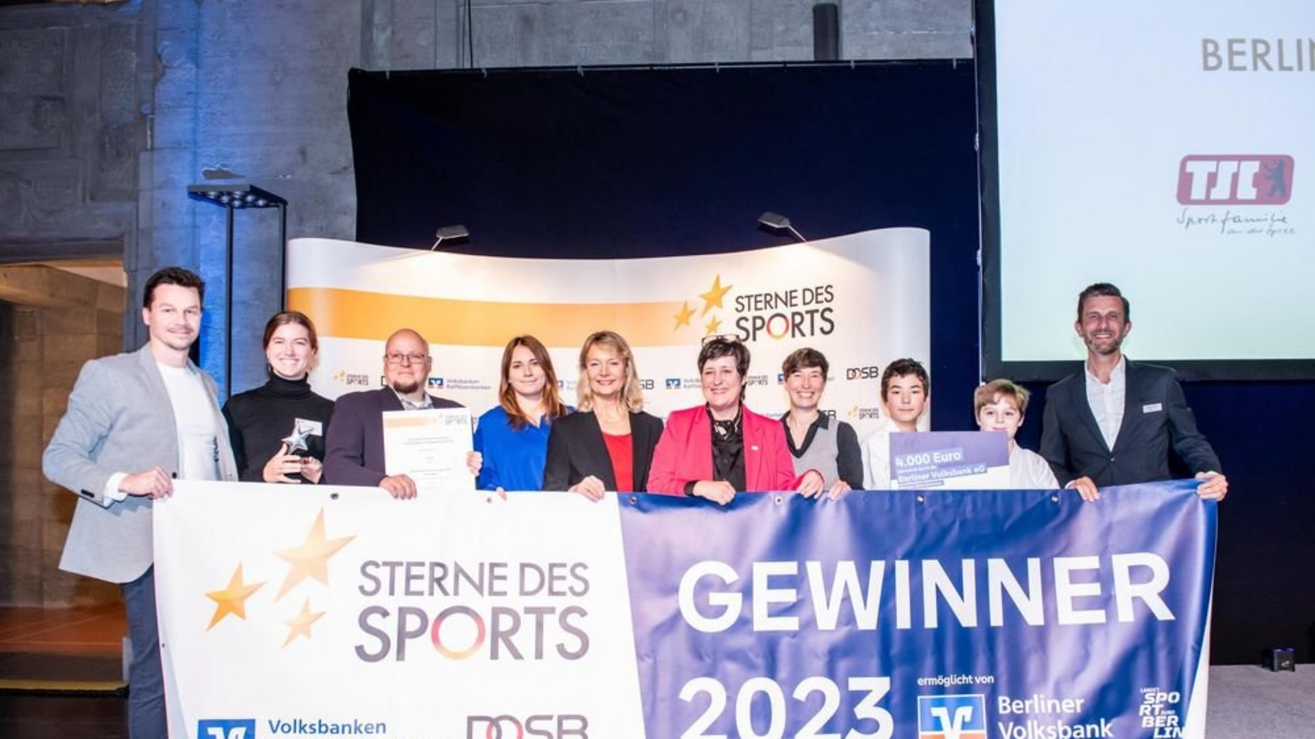 Gewinner der Sterne des Sports stehen hinter einem Gewinner-Plakat und halten dieses vorm Körper