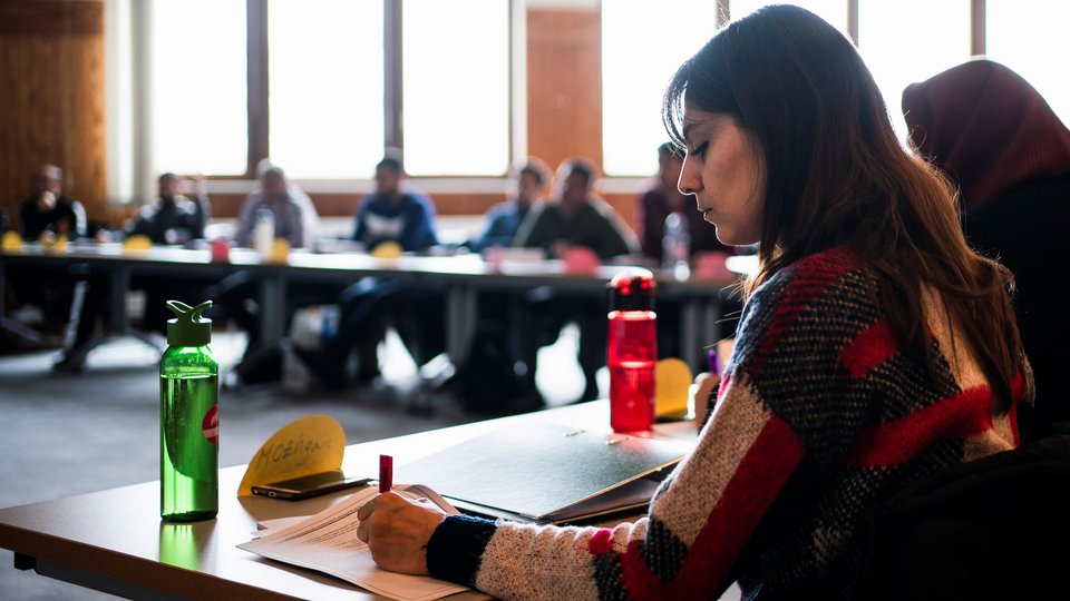 Frau sitzt an Tisch und schreibt etwas.