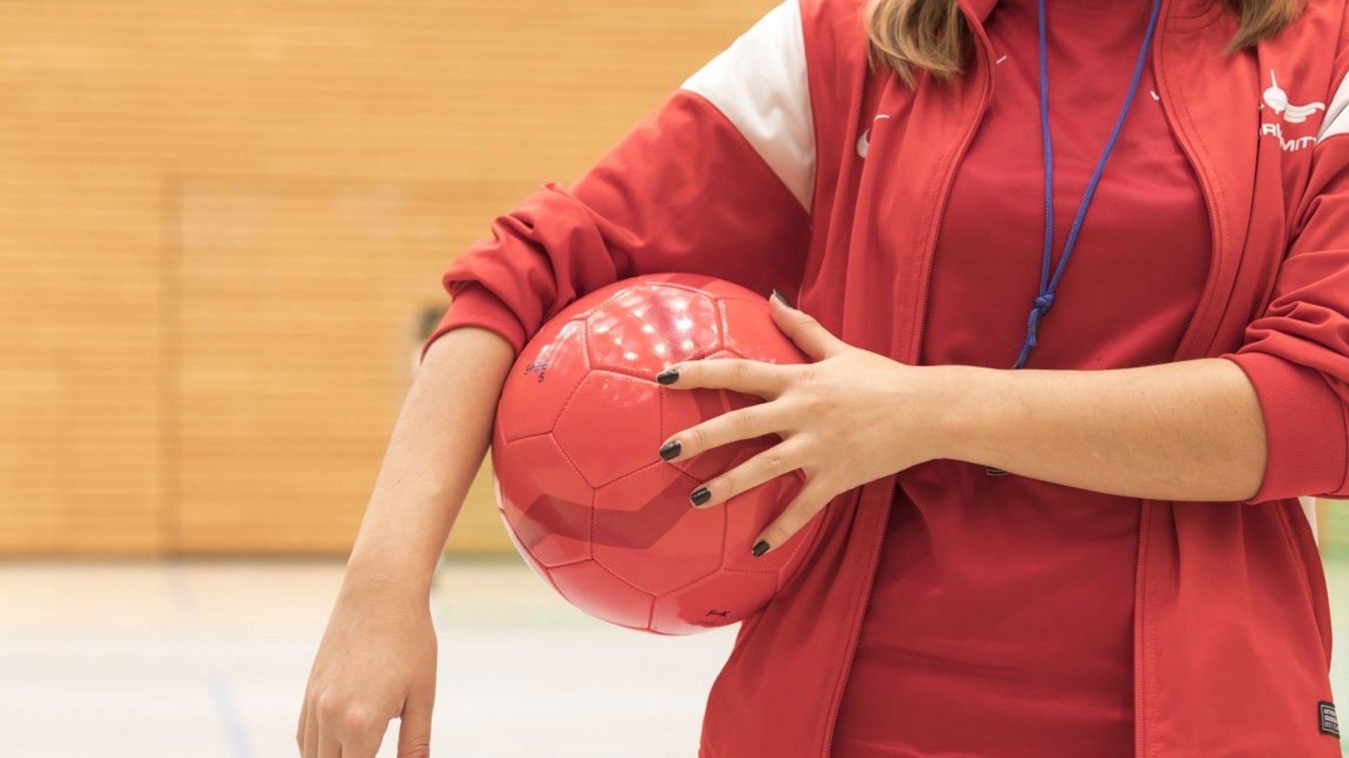 Das Bild zeigt einen roten Ball, den eine Übungsleiterin unter den Arm geklemmt hat.